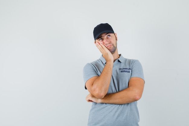 Young technician in grey uniform leaning cheek on hands,thinking about something and looking amused.