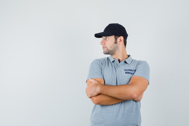 Young technician in grey uniform standing with crossed arms and looking focused.