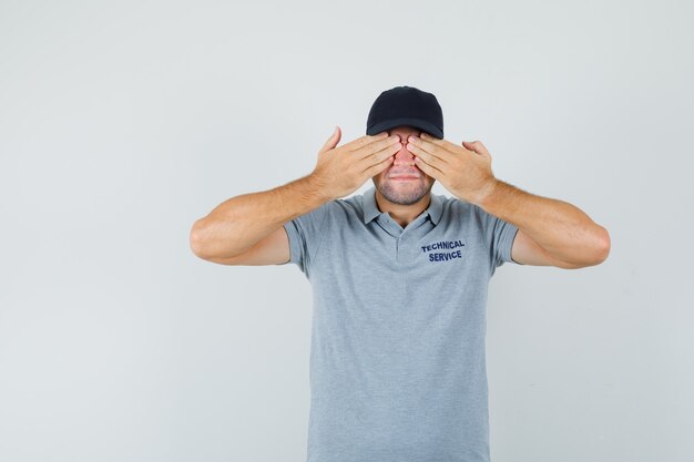 Young technician keeping hands on eyes in grey uniform and looking excited.