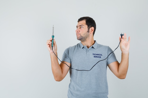 Young technician looking at screwdriver holding his hand in grey uniform and looking focused.