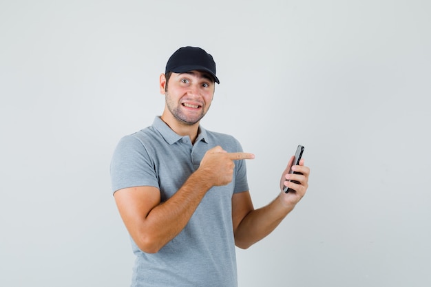 Young technician pointing at mobile phone in grey uniform and looking cheerful.