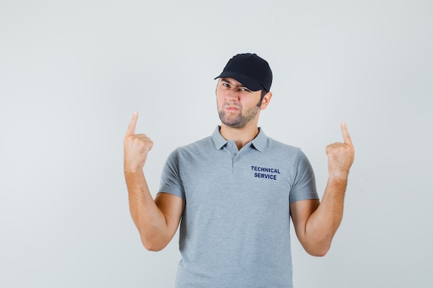 Free photo young technician pointing up in grey uniform and looking hesitant.