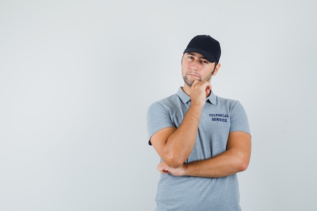 Young technician propping chin on hand in grey uniform and looking hesitant.