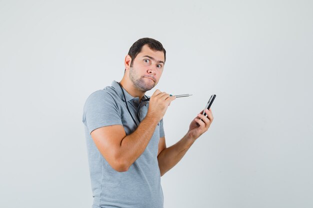 Young technician trying to open the back of his smartphone by using drill in grey uniform and looking curious.