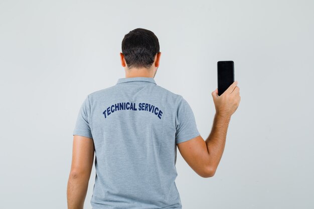 Young technician turning backward and showing his phone in grey uniform and looking elegant.