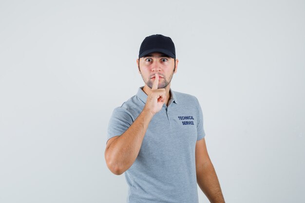 Young technician in uniform showing silence gesture and looking careful.