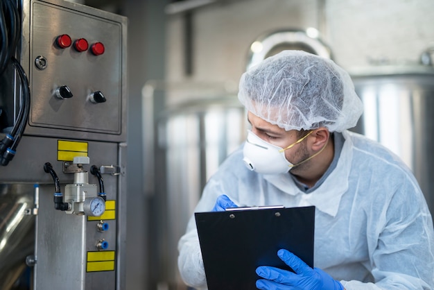 Free Photo young technologist in white protective uniform controlling industrial machine at production plant