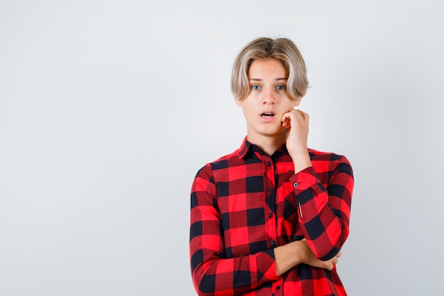 Free photo young teen boy in checked shirt touching jaw and looking confused , front view.