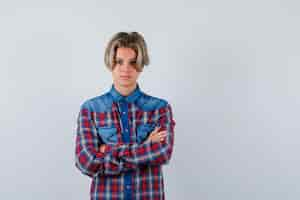 Free photo young teen boy keeping arms folded in checked shirt and looking serious. front view.