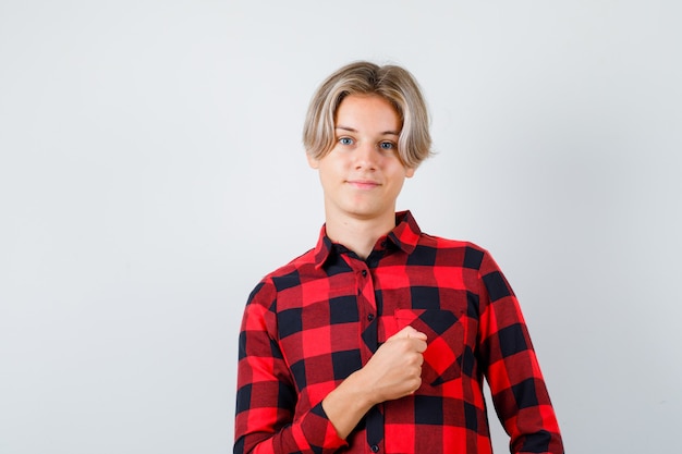 Free photo young teen boy keeping fist over chest in checked shirt and looking confident , front view.