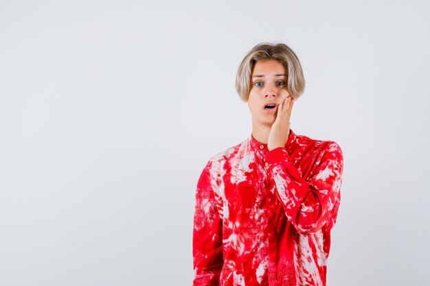 Young teen boy keeping hand on cheek in shirt and looking disappointed. front view.