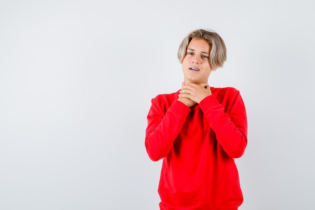 Young teen boy suffering from sore throat in red sweater and looking bothered. front view.