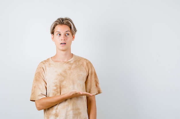 Young teen boy in t-shirt pretending to show something, rolling eyes and looking focused , front view.