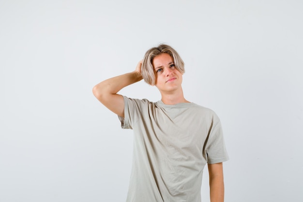 Young teen boy in t-shirt scratching head while looking up and looking pensive , front view.