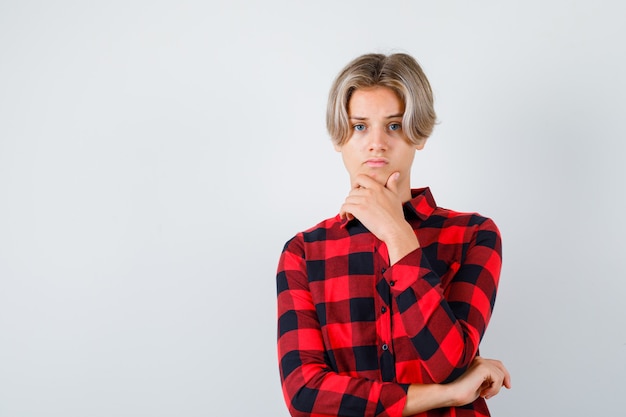 Free photo young teen boy with hand on chin in checked shirt and looking sad , front view.