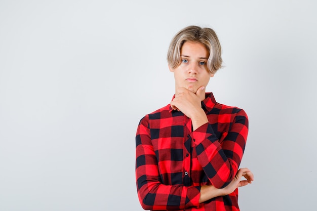 Free photo young teen boy with hand on chin in checked shirt and looking upset. front view.