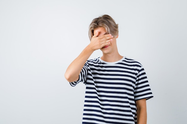 Young teen boy with hand on face in striped t-shirt and looking ashamed. front view.