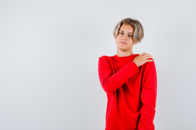 Young teen boy with hand on shoulder in red sweater and looking tired. front view.