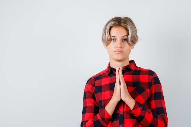 Free photo young teen boy with hands in praying gesture in checked shirt and looking hopeful , front view.