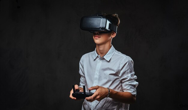 Young teenager dressed in a white shirt wears virtual reality glasses and controls the quadcopter using the control remote.