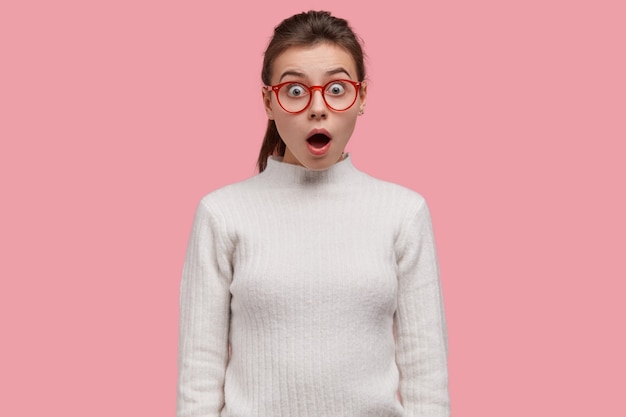 Free photo young teenager stands in stupor at shocking scene, wears spectacles and casual outfit, being speechless and upset