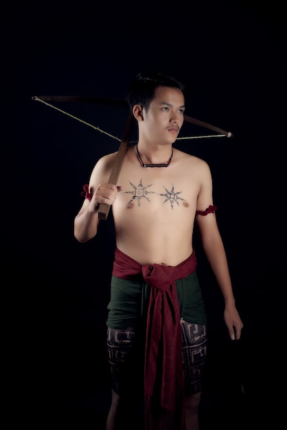 Free Photo young thailand male warrior posing in a fighting stance with a crossbow