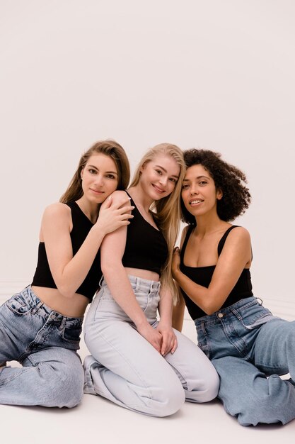 Young three interracial ladies brunette blonde and fairhaired in casual clothes are sitting on white background together