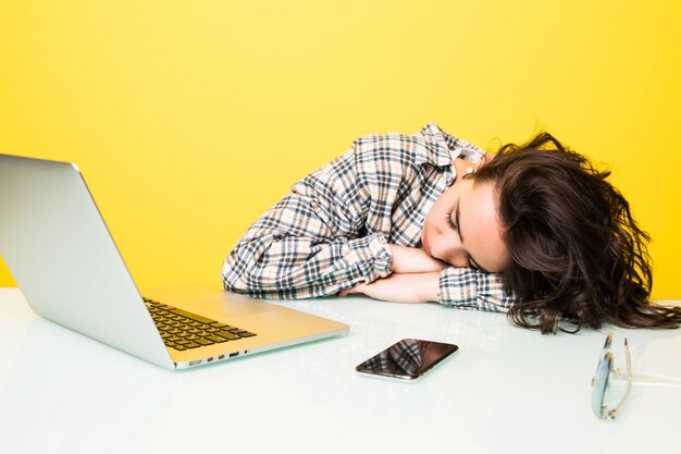 Young tired woman working on laptop isolated on yellow wall