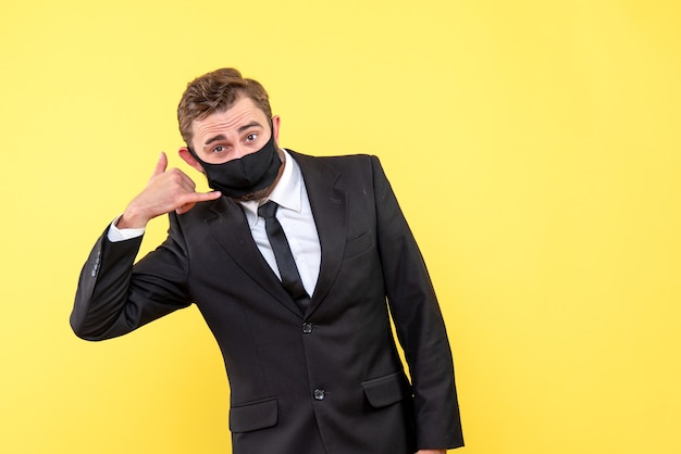 Free photo young trader with medical mask showing the contact me gesture on yellow