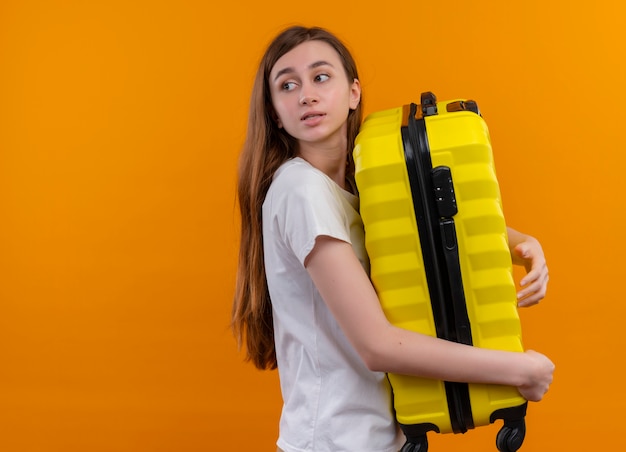 Free Photo young traveler girl holding suitcase looking at left side on isolated orange wall with copy space