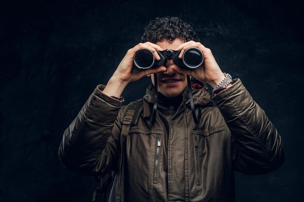 The young traveler looks into the camera with binoculars and smiles on black background