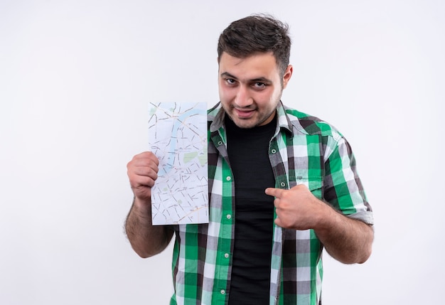 Free photo young traveler man in checked shirt holding map pointing with finger to it looking confident standing over white wall