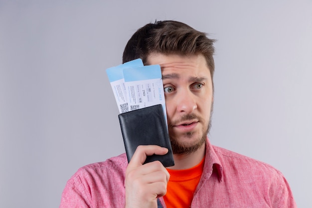 Young traveler man holding air tickets looking aside with confuse expression on face over isolated white background