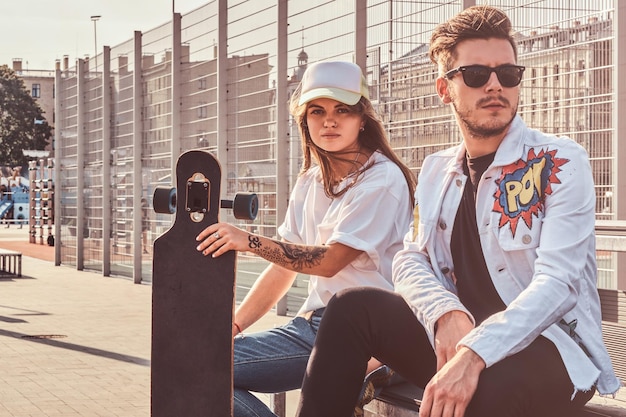 Free Photo young trendy couple is chilling on the sunny street with their longboards. they wear denim.