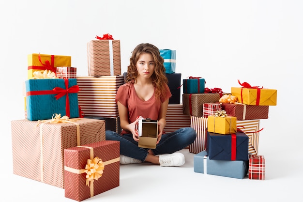 Free Photo young upset curly woman sitting on floor among gift boxes showing one she opened is empty