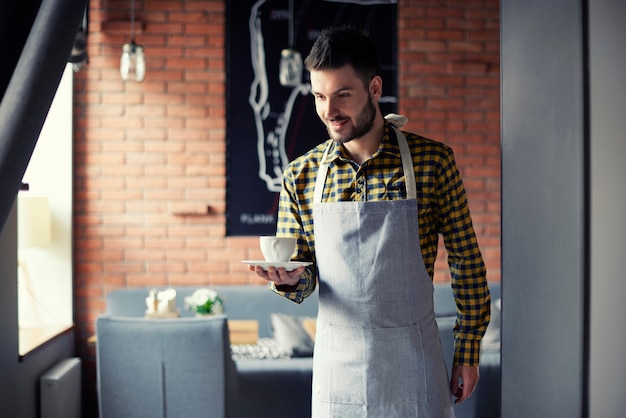 Free photo young waiter serving cup of coffee