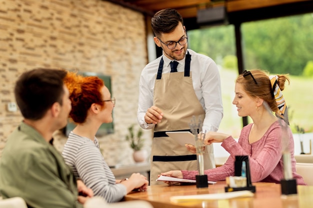 Free photo young waiter showing menu on touchpad to his customers in a cafe