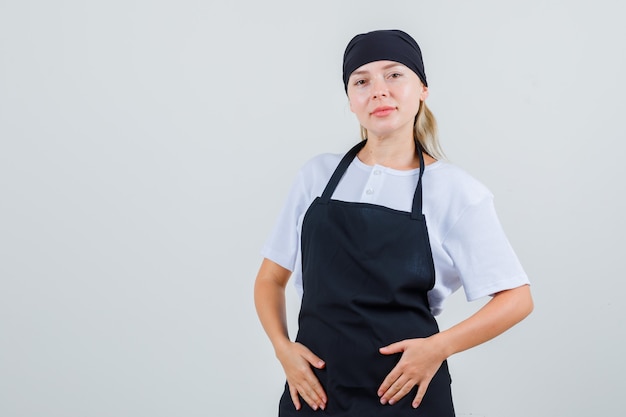 Young waitress holding hands on her apron in uniform and looking optimistic