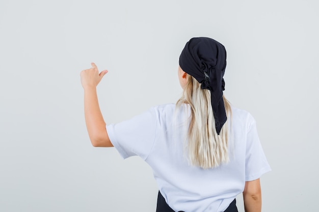 Free photo young waitress pointing at something in uniform and apron back view.