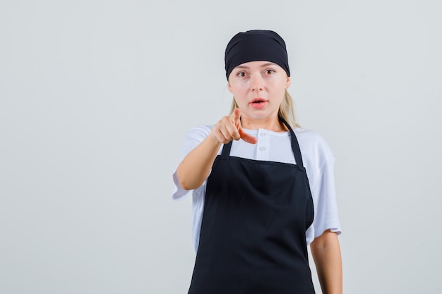 Free photo young waitress pointing in uniform and apron and looking amazed