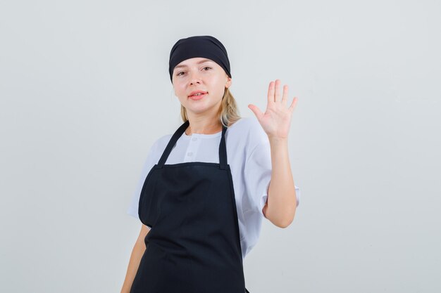 Young waitress showing palm and smiling in uniform and apron