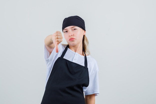 Free photo young waitress showing thumb down in uniform and apron front view.