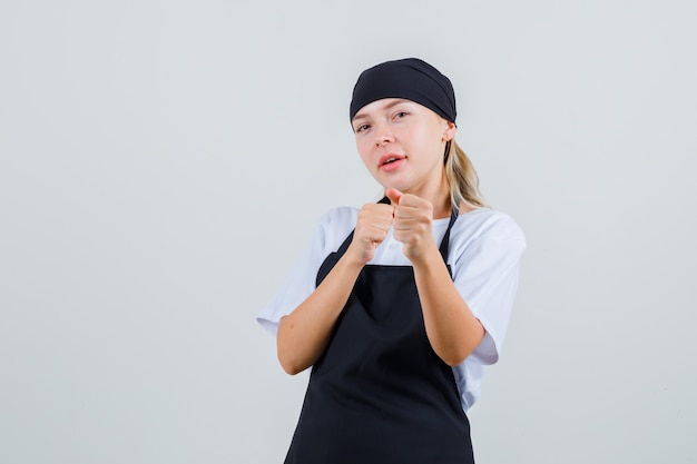 Young waitress in uniform and apron standing in fight pose and looking confident