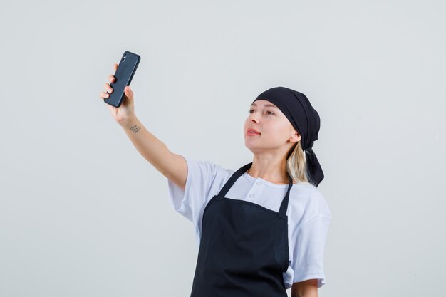 Young waitress in uniform and apron taking selfie on mobile phone