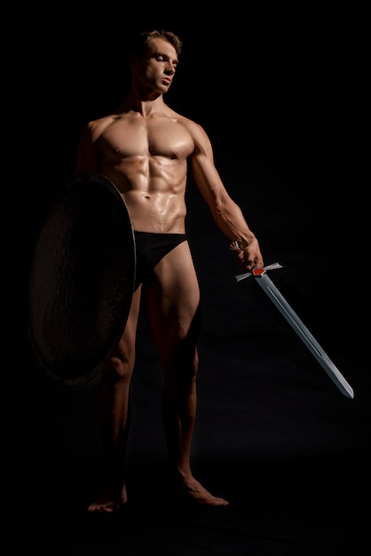 Young warrior with shield isolated on black.