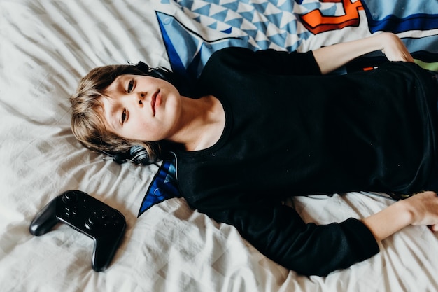 Free photo young white boy laying on his bad with a wireless controller