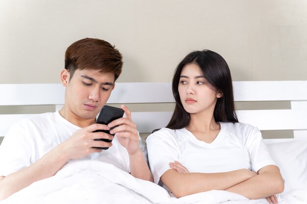 young wife sitting on bed with feeling upset her husband use smartphone in napping time