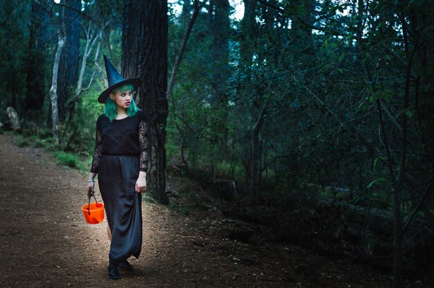 Young witch with basket standing in forest