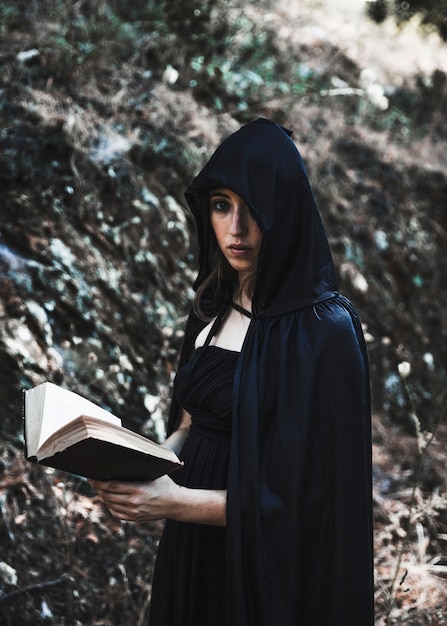 Young witch with book in thicket