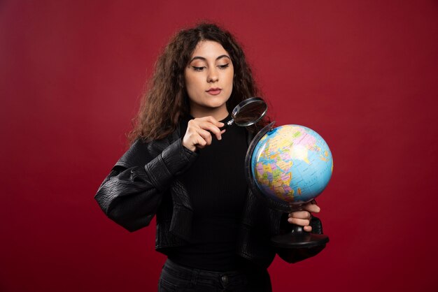 Young woman in all black outfit holding a globe with loupe.